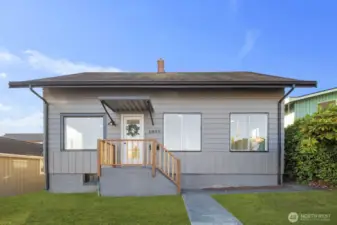 Inviting exterior with horizontal siding, covered entry, and a simple wood-railed porch surrounded by a neatly maintained lawn.