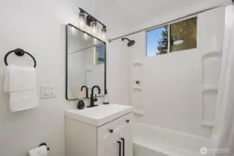 Updated full bath with a white vanity, black fixtures, framed mirror, and shower-tub combination with built-in shelving.