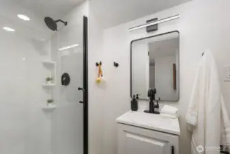 Modern bath with a walk-in shower, glass enclosure, black fixtures, and a white vanity with matching framed mirror.