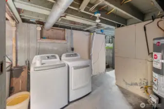 Alternate angle of the lower-level space showing washer and dryer placement, exposed beams, and access to the exterior.