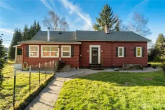 A charming front entrance welcomes you home with classic farmhouse character. A defined walkway with a gate leads to the front door, framed by mature landscaping and a level lawn that reinforces the home’s peaceful, open setting.