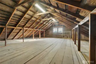 A spacious loft area above the three-car garage, offering an impressive amount of open, usable space. Exposed beams and vaulted lines create a wide-open feel, while solid flooring and overhead lighting make it practical for storage, hobbies, or workspace use. With plumbing located directly below, this area also presents flexibility for future improvements, whether expanding storage, creating a workshop, or finishing additional space to suit changing needs.