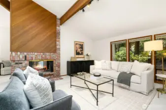 Walls of windows flood the living room with natural light, highlighting warm cedar paneling and the striking double-sided fireplace — a true nod to Northwest mid-century design.