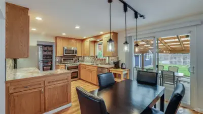 Bright kitchen and dining space showcasing warm wood cabinetry, stainless steel appliances, and stylish pendant lighting.