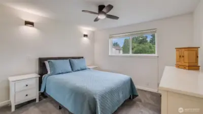 Bright and inviting primary bedroom featuring a large window, modern ceiling fan light and wall sconces, and a serene atmosphere.