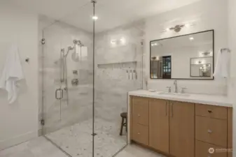 Full glass shower with marble tile and two separate vanities.