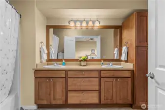 En suite bath featuring dual sinks, wood cabinetry, and shower/tub combo