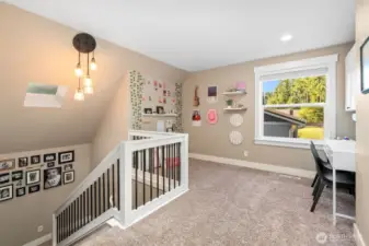 At the top of the stairs, this loft offers a bright, flexible space perfect for an office, homework zone, or quiet retreat. The large window overlooks the front lawn and driveway, letting in plenty of natural light. Warm oatmeal carpeting keeps things cozy, while the skylight above the staircase adds a fresh, airy touch.