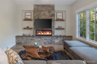 Warm and inviting living room centered around a striking floor-to-ceiling stone fireplace with built-in shelving and electric flame insert—perfect for cozy island evenings.