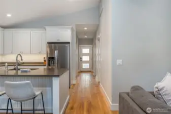 Functional layout connects kitchen to the main entry and hallway, featuring wide plank wood flooring and clean modern finishes throughout.