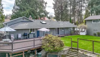 The back of the house opens to a lush mature landscape, a beautiful very spacious deck extends from the rear, providing the perfect spot for lounging, dining, and entertaining guests against a backdrop of flowering shrubs and trees.