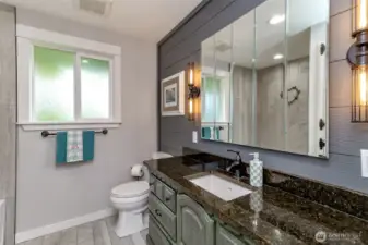 Completely remodeled bathroom featuring a gorgeous vanity and countertops, a shiplap accent wall, elegant lighting, and beautiful tile flooring