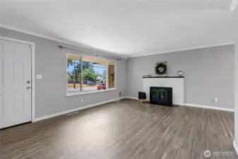 This spacious living room is bathed in natural light from the large front window and anchored by a painted brick fireplace—perfect for cozy evenings. Neutral tones provide a warm, welcoming feel while giving buyers a versatile backdrop for décor.