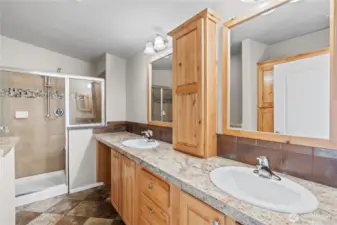 Beautifully upgraded primary bathroom featuring dual sinks, natural wood cabinetry, and a spacious walk-in shower with stylish tile accents. This luxurious ensuite adds both comfort and convenience to this energy-efficient home in Lacey’s 55+ Lakeview Meadows community.