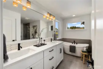 Large primary bathroom with large-scale tiled floors, a soaking tub, shower with frameless glass and dual sinks with white and grey marble-look quartz countertops.