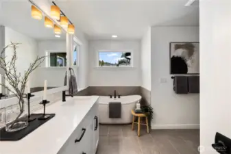 Large primary bathroom with large-scale tiled floors, a soaking tub, shower with frameless glass and dual sinks with white and grey marble-look quartz countertops.