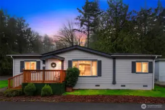Charming curb appeal with a welcoming front porch and lush greenery set against a backdrop of tall evergreens.