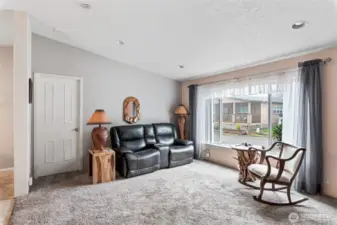 Bright and inviting living room with large windows, plush carpet, and cozy ambiance.