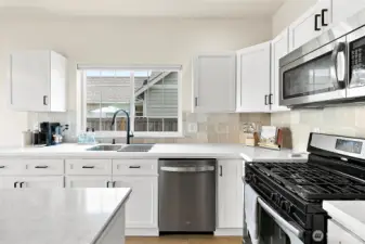 Sleek quartz countertops, a striking glass tile backsplash, and premium stainless steel appliances elevate the kitchen with a fresh, modern look.