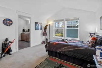 Bright upper-level bedroom with vaulted ceiling, large windows, and en suite bath access.