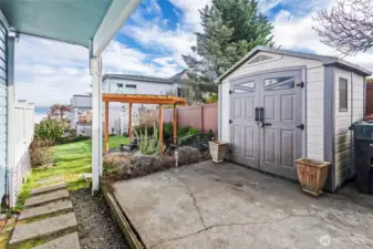 A garden shed and patio are set at the end of the driveway. Stepping stones lead to the lawn and pergola.