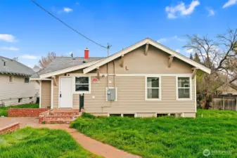 Back of home with spacious backyard and brick patio/walkway.