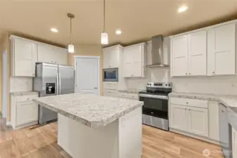 Beautifully tiled backsplash enhances the look of the stark white cabinetry and brush nickle finishes.  Plenty of lighting with the canned lights and pendant lighting over the island.