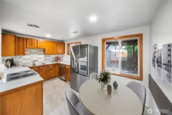 This bright kitchen features warm wood cabinetry, stainless steel appliances, and a dining area with a view of the backyard. *virtually staged*