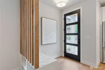 This entryway blends warmth and modernity with a black-panel glass front door that invites natural light, while the slatted wood partition and built-in bench create a functional yet artful transition into the home.