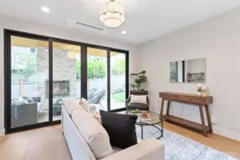 This inviting outdoor living space extends seamlessly from the interior, framed by large sliding glass doors and anchored by a built-in fireplace—perfect for cozy evenings or relaxed entertaining. Surrounded by greenery and enclosed for privacy, it offers a tranquil retreat with all-season appeal.