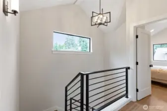 This upper landing blends clean lines and natural light with a sleek metal railing and geometric pendant—offering a quiet transition space with modern character.