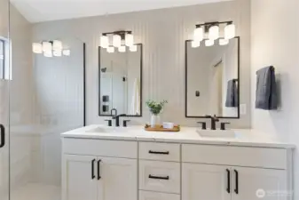 This modern bathroom features a double vanity with black-framed mirrors and sleek hardware, balanced by a glass-enclosed shower and soft natural accents for a clean, symmetrical look.