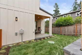 This inviting backyard features a covered patio with a warm stone fireplace, cozy seating, and a lush lawn—perfect for relaxing or entertaining in style.