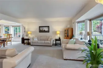 Elegant living room featuring large windows that allow abundant natural light to illuminate the space while providing picturesque views of the outdoors. Conveniently connected to the dining room and entry, this inviting space is perfect for entertaining guests with ease and style.