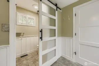 The WC is separated from the rest of the bathroom with an attractive barn door.  Wainscotting adds to the pleasing decor.