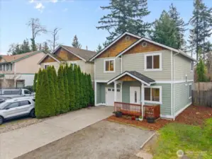 Angled exterior view highlighting the home’s gabled rooflines, covered porch, and attached garage. Tall evergreen hedges along the side add greenery and privacy.
