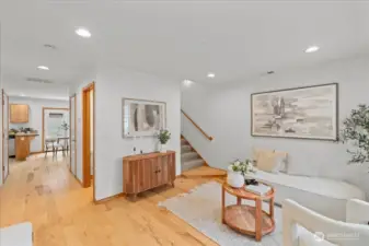 Comfortable living space with natural light from the front window and views toward the entry door. Open layout leads to the hallway and kitchen beyond.