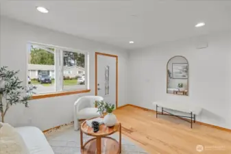 Bright entry living space with laminate flooring and recessed lighting. Open layout offers clear sightlines toward the hallway and staircase.