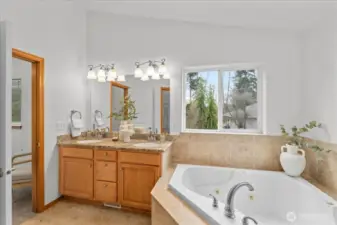 Spacious primary bathroom with dual-sink vanity, granite counters, soaking tub, and tiled flooring. Large window provides natural light and outdoor views.