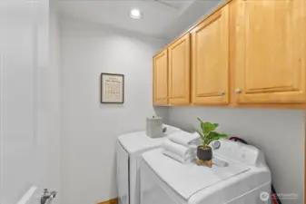 Laundry room with side-by-side washer and dryer and overhead wood cabinetry for additional storage. Bright recessed lighting and neutral walls create a clean, functional workspace.
