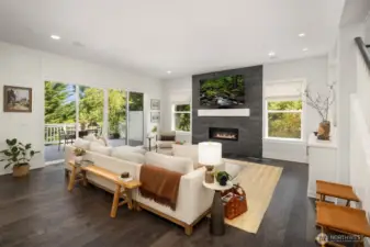 The heart of the main floor showcases a chef-inspired kitchen with an oversized white island and premium appliance suite, flowing effortlessly to a covered outdoor entertaining deck with inviting fireplace.