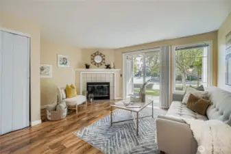 Bright and inviting living room features a cozy wood-burning fireplace, perfect for relaxing evenings. Freshly painted walls and beautiful laminate flooring create a warm, modern feel. Large windows and sliding glass doors flood the space with natural light and provide easy access to the patio—ideal for indoor-outdoor living.