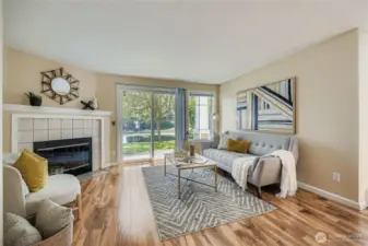 Bright and inviting living room features a cozy wood-burning fireplace, perfect for relaxing evenings. Freshly painted walls and beautiful laminate flooring create a warm, modern feel. Large windows and sliding glass doors flood the space with natural light and provide easy access to the patio—ideal for indoor-outdoor living.