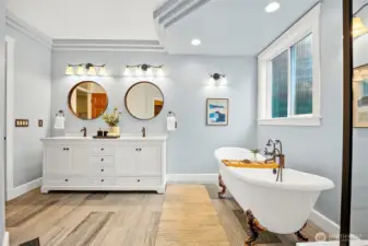 Primary en-suite bathroom facing double-sink farmhouse vanity with clawfoot soaking tub.