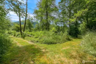 Extra wide groomed trail system throughout, seen here, leading to the lower pasture, outbuilding, greenhouse frame, power meter and incredible pond.