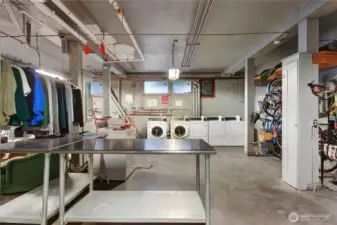 Basement laundry with multiple machines, folding tables and sitting area.