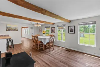 Sunlit Dining Area with Exposed Beams & Scenic Views  Enjoy meals bathed in natural light in this charming dining room featuring rustic exposed log beams, wood-style flooring & large windows that frame peaceful views of the surrounding acreage. Whether you’re gathering for family dinners or hosting guests, this space offers warmth, character & a connection to the outdoors. With direct sightlines to the kitchen & porch, it’s the perfect setting for everyday comfort & country-style living in the Pacific Northwest.