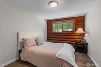 Cozy Bedroom with Log Accent Wall & Natural Light  This charming bedroom blends cabin comfort with modern simplicity, featuring a striking log wall accent that adds warmth & texture to the space. A large window invites in natural light & views of the surrounding trees, while neutral tones & updated flooring create a peaceful, restful atmosphere. Whether used as a guest room or personal retreat, this space offers the perfect blend of rustic charm & cozy serenity in a true Pacific Northwest setting.