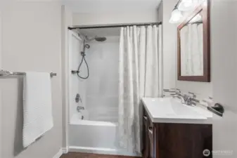 Charming Upper-Level Bathroom  Fresh, functional, and full of style—this upstairs bathroom features a full-size tub with a rainfall showerhead, sleek tile accents, and a modern vanity with rich wood cabinetry. Perfectly placed for easy access to all upstairs bedrooms, it's both beautiful and practical.