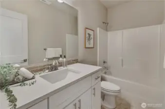 The bathroom area includes white cabinetry, easy to clean quartz surfaces with below mounted sink and tub-shower
